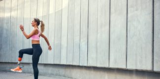 Ženska s športno protezo teče na prostem ob stavbi.