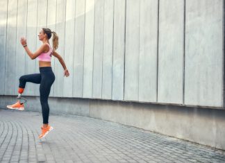 ABC programi športa za invalide Ženska s športno protezo teče na prostem ob stavbi.