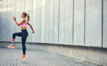 Ženska s športno protezo teče na prostem ob stavbi.