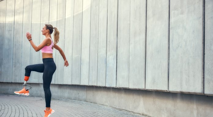 Ženska s športno protezo teče na prostem ob stavbi.