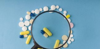 Povečevalno steklo nad različnimi tabletami in kapsulami, simbol previdnosti pri nakupu zdravil preko spleta