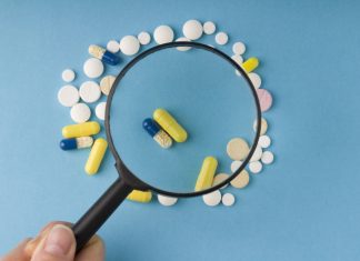 Povečevalno steklo nad različnimi tabletami in kapsulami, simbol previdnosti pri nakupu zdravil preko spleta