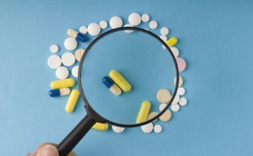 Povečevalno steklo nad različnimi tabletami in kapsulami, simbol previdnosti pri nakupu zdravil preko spleta